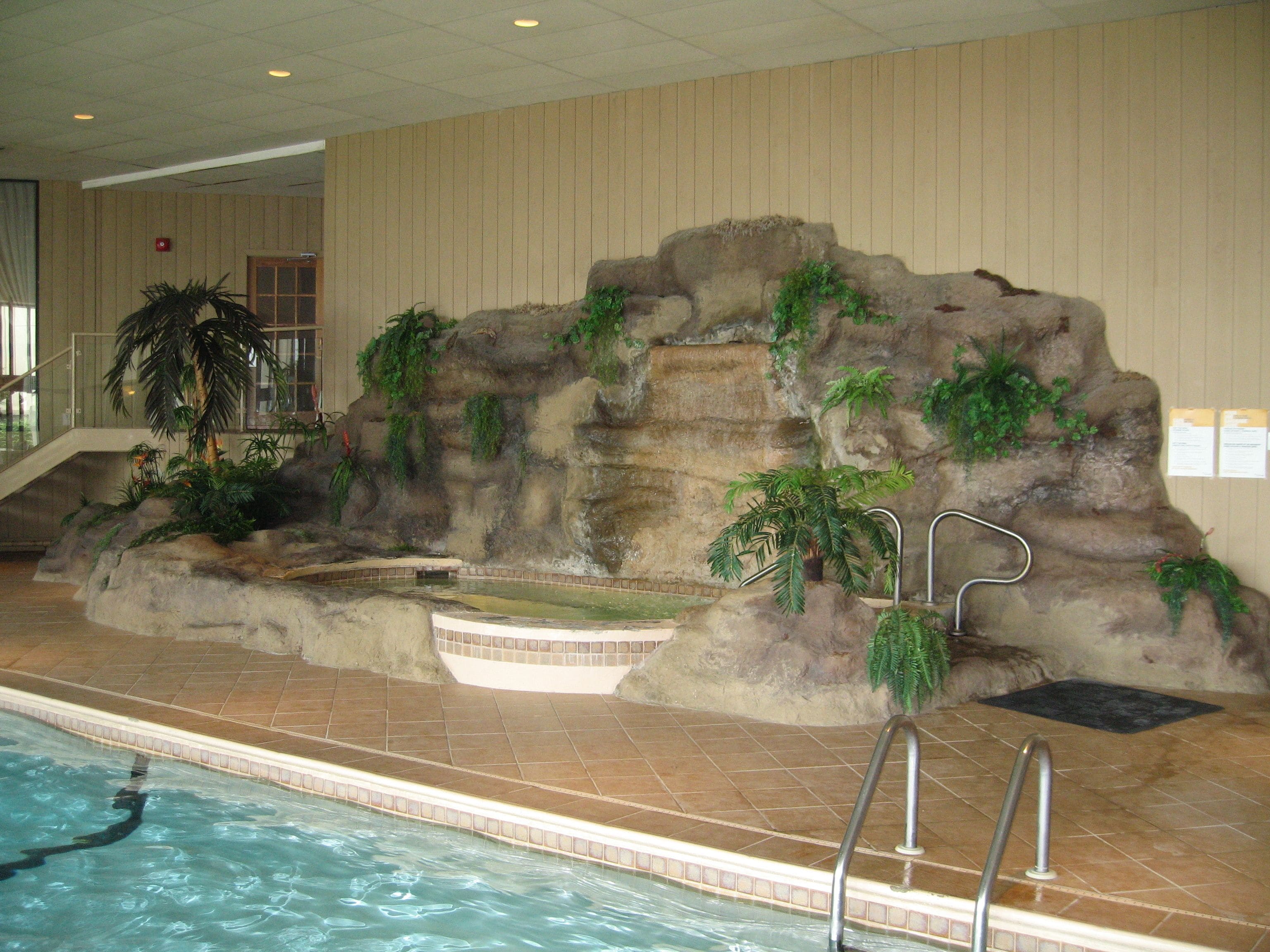Una piscina interior con un paisaje artificial rocoso, una palmera y una pequeña cascada.