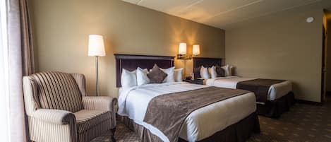 A hotel room with two beds, a chair, and a lamp.