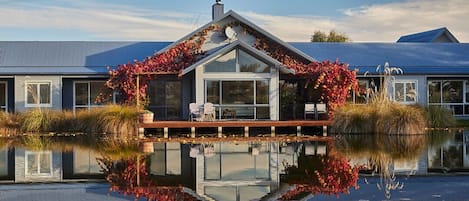 A modern house with a glass front, a deck, and a reflection in the water.