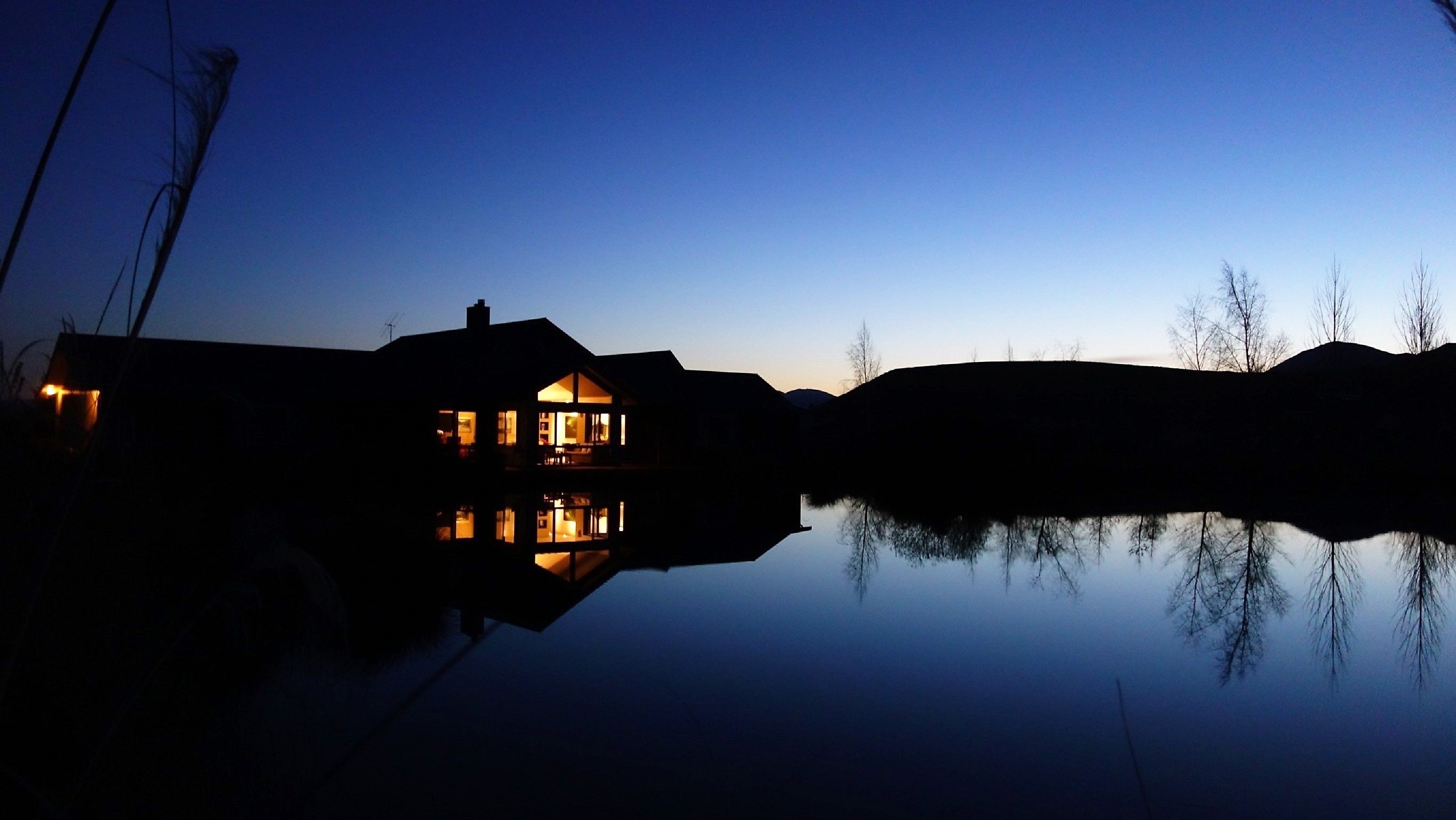 Een huis met een groot raam en een opvallende schoorsteen, dat weerspiegelt in een rustig waterlichaam.