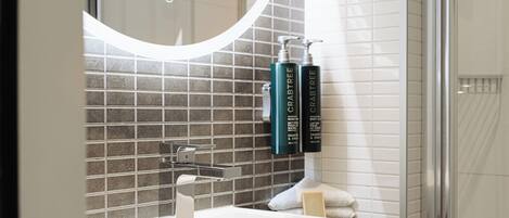 A bathroom with a white sink, a mirror with a circular light, and two bottles of Crabtree body wash on the wall.