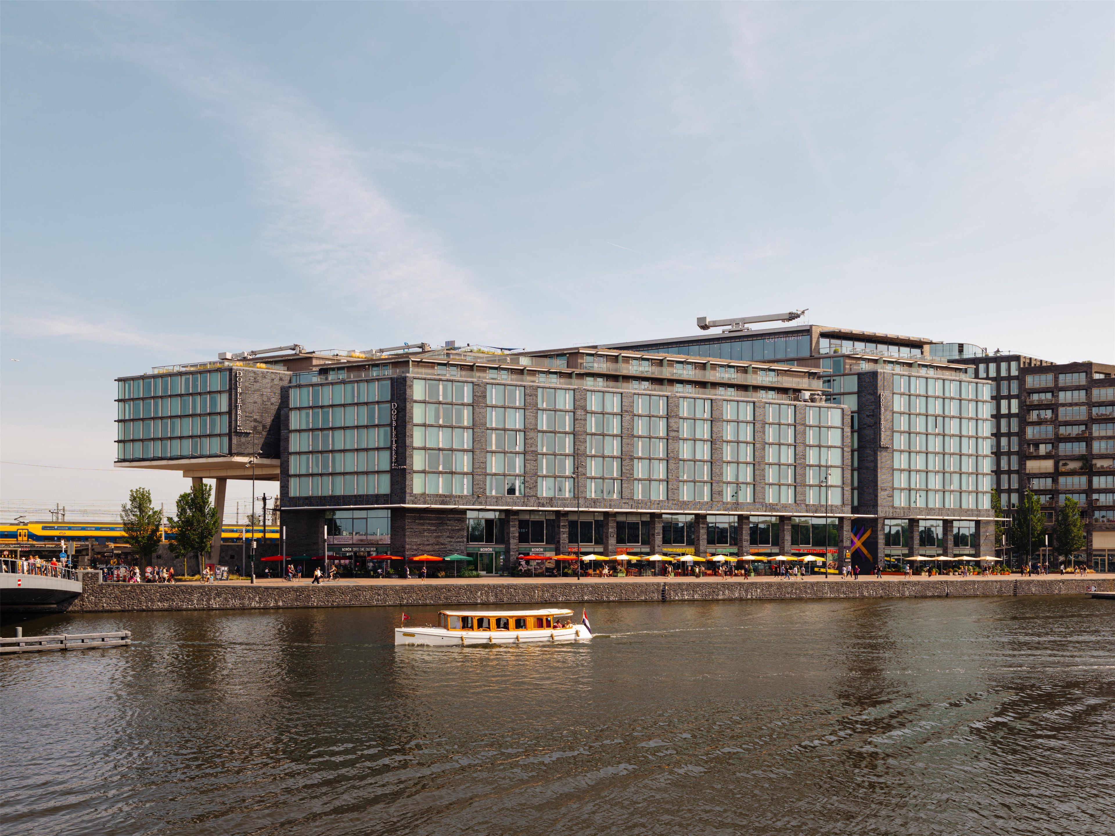 Un hotel moderno con fachada de vidrio, vistas al agua y un muelle para embarcaciones.