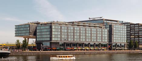 Un hotel moderno con fachada de vidrio, vistas al agua y un muelle para embarcaciones.