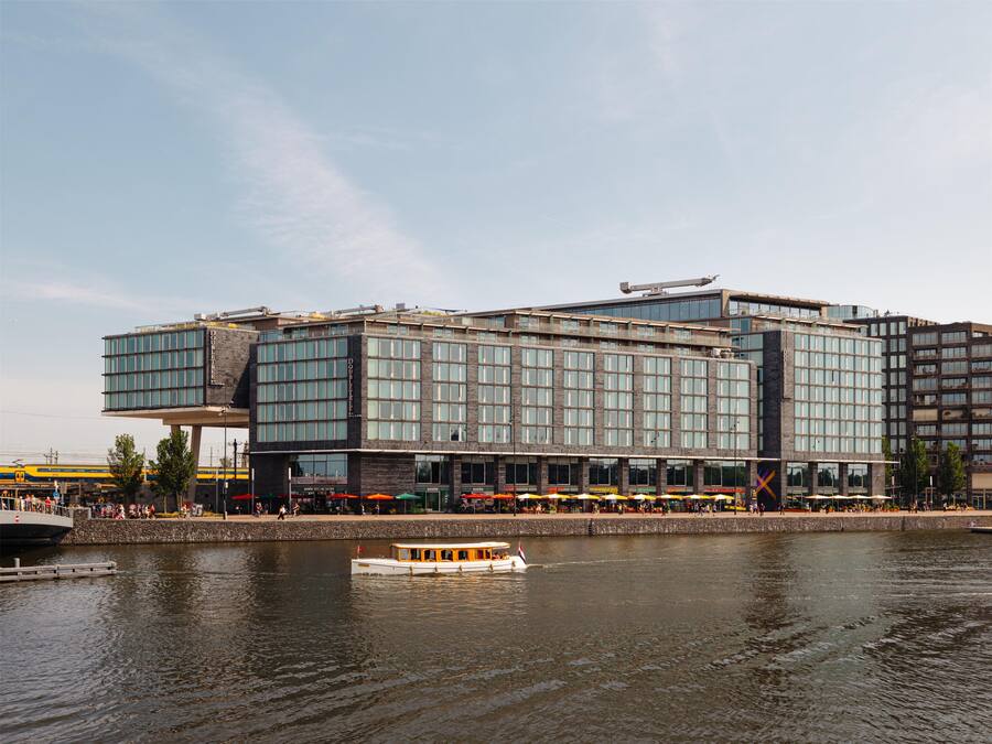 Un hôtel moderne doté d’une façade en verre, offrant une vue sur le front de mer et comprenant un quai pour bateaux.