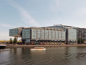 Un hotel moderno con fachada de vidrio, vistas al agua y un muelle para embarcaciones.
