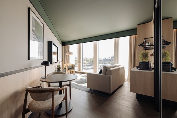 Una habitación de hotel moderna con zona de comedor, sofá y vistas a la ciudad.