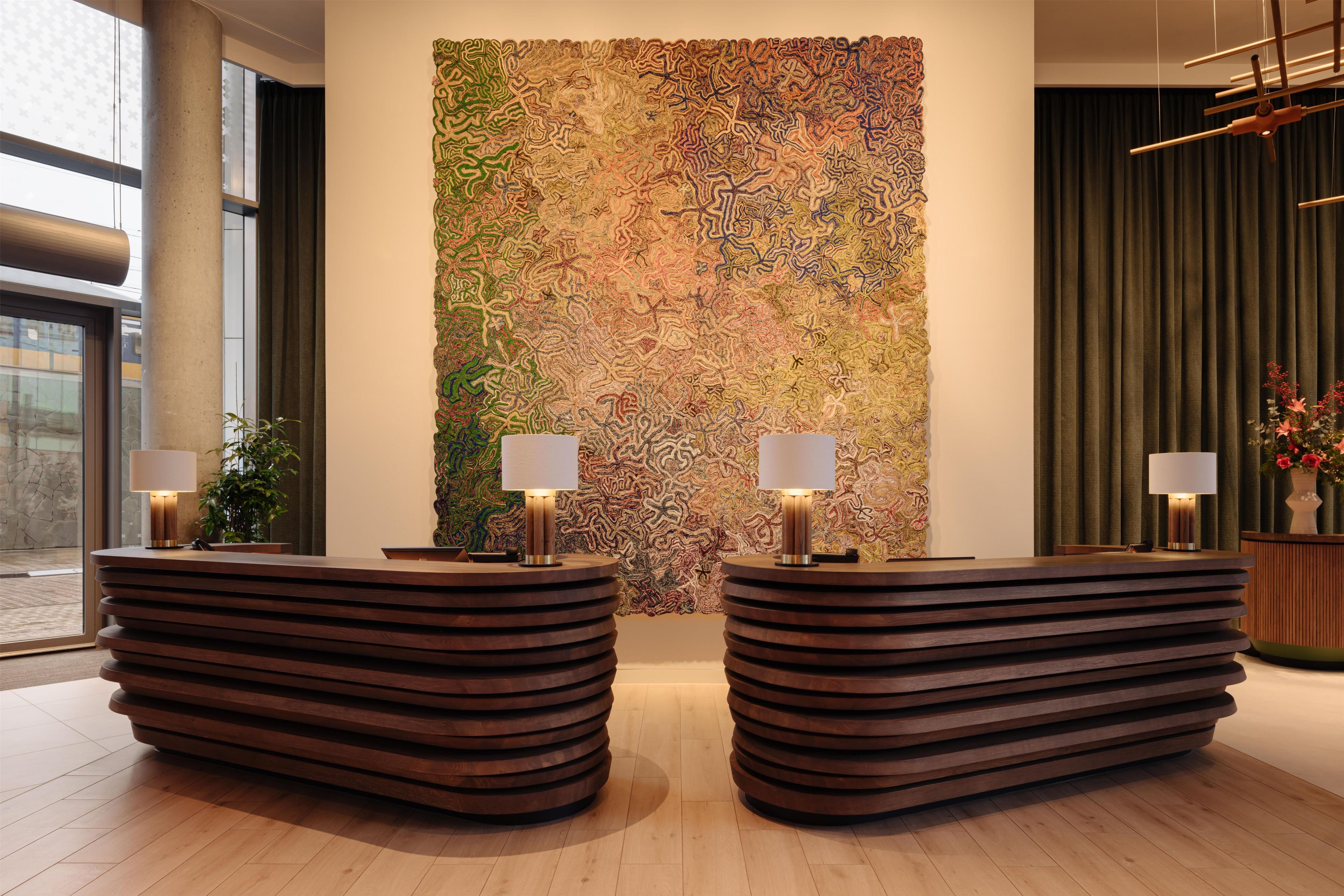 Zona de recepción con dos mostradores de madera, un gran cuadro abstracto en la pared y un fondo de cortina verde.