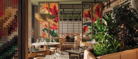 En restaurantindretning med runde borde, polstrede siddepladser og store blomsterbilleder på væggene.