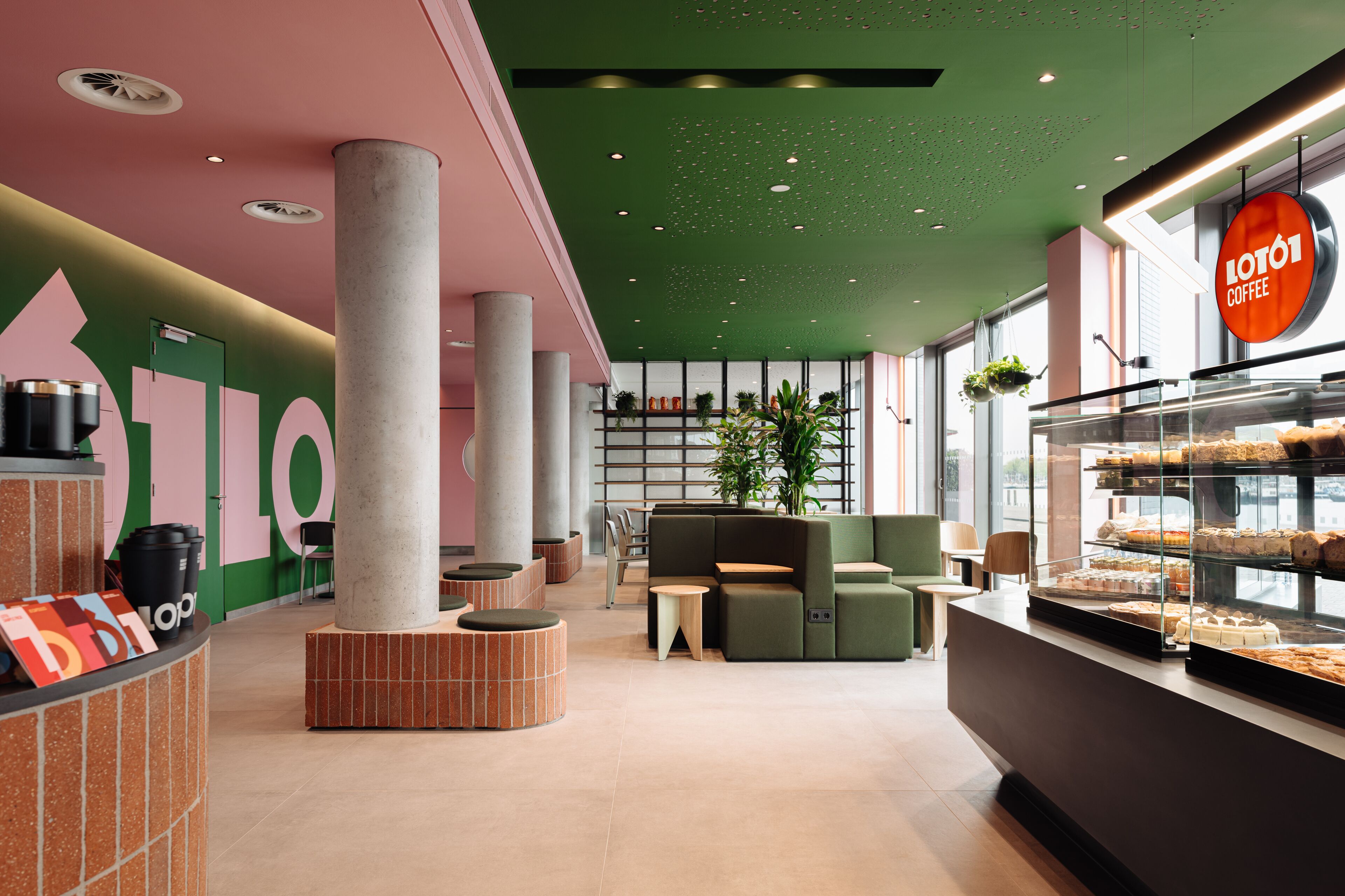 Een modern caféinterieur met een groen plafond, zithoeken en een vitrine met gebak.
