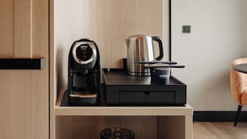 Uma cozinha compacta com cafeteira, chaleira e duas xícaras em uma prateleira de madeira.