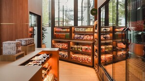 A modern interior with a wooden counter, shelves stocked with snacks, and a large window offering a view of the outside.
