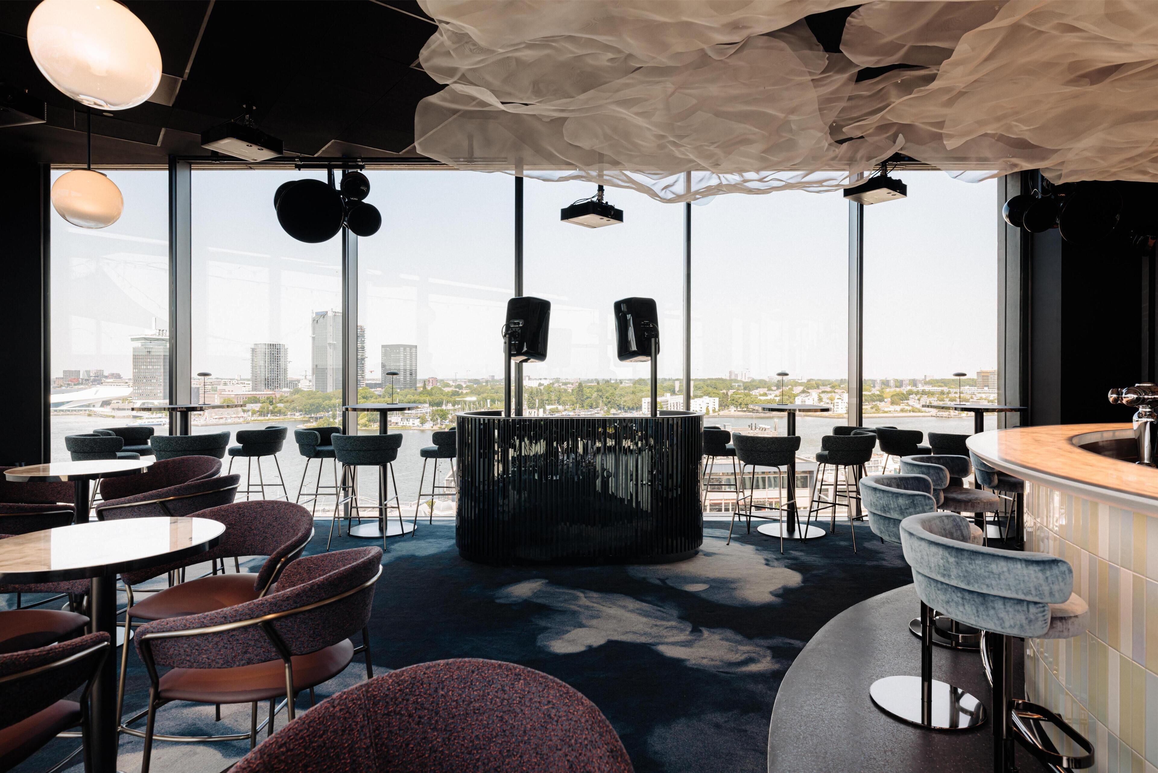Eine moderne Bar mit Stadtblick, runden Tischen und Barhocker.