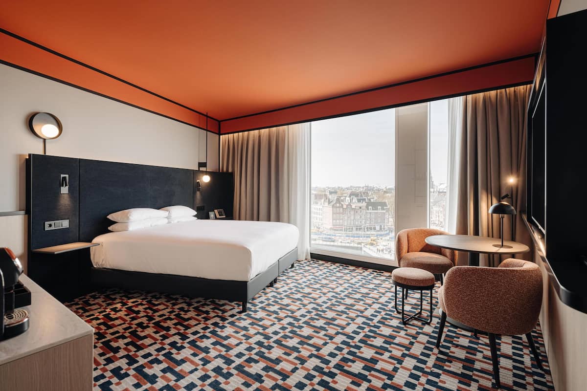 A hotel room with a large bed, a desk with a coffee machine, a round table, and a chair.