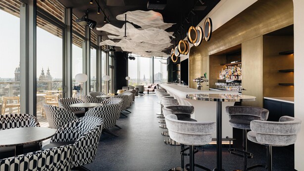 A bar area with high stools, a long counter, and a view of a cityscape through large windows.