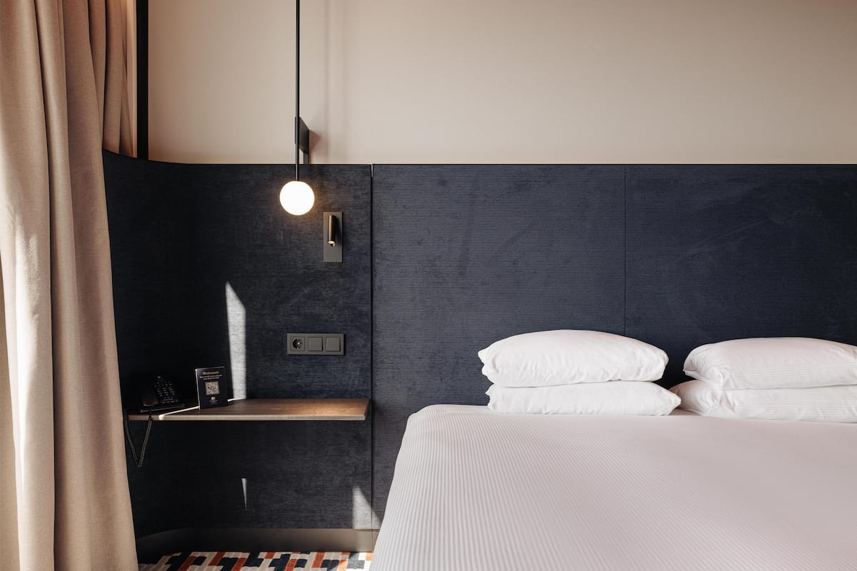 A hotel room with a bed, bedside table, lamp, and curtains.
