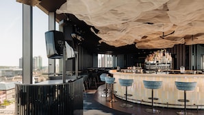 A modern bar area with a curved counter, bar stools, and a city view.