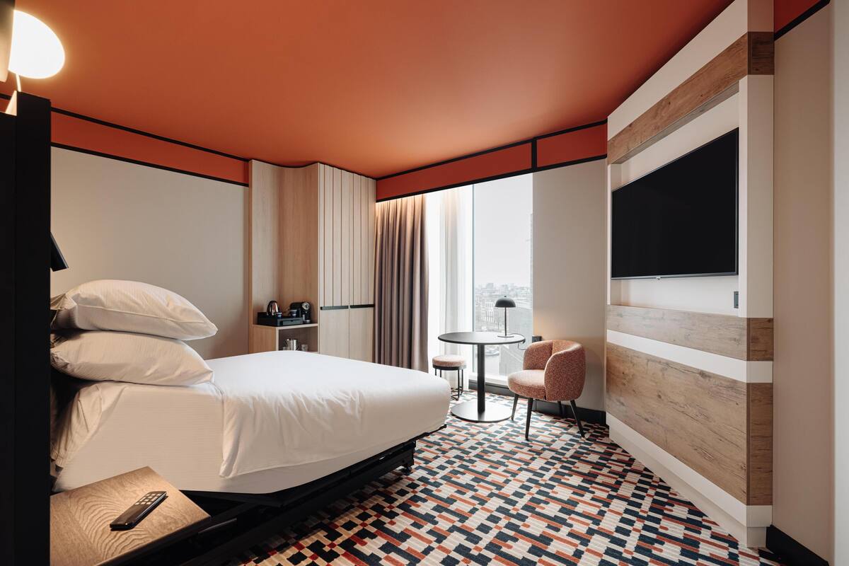 A hotel room with a large bed, a round table, a chair, a TV, and a window with curtains.