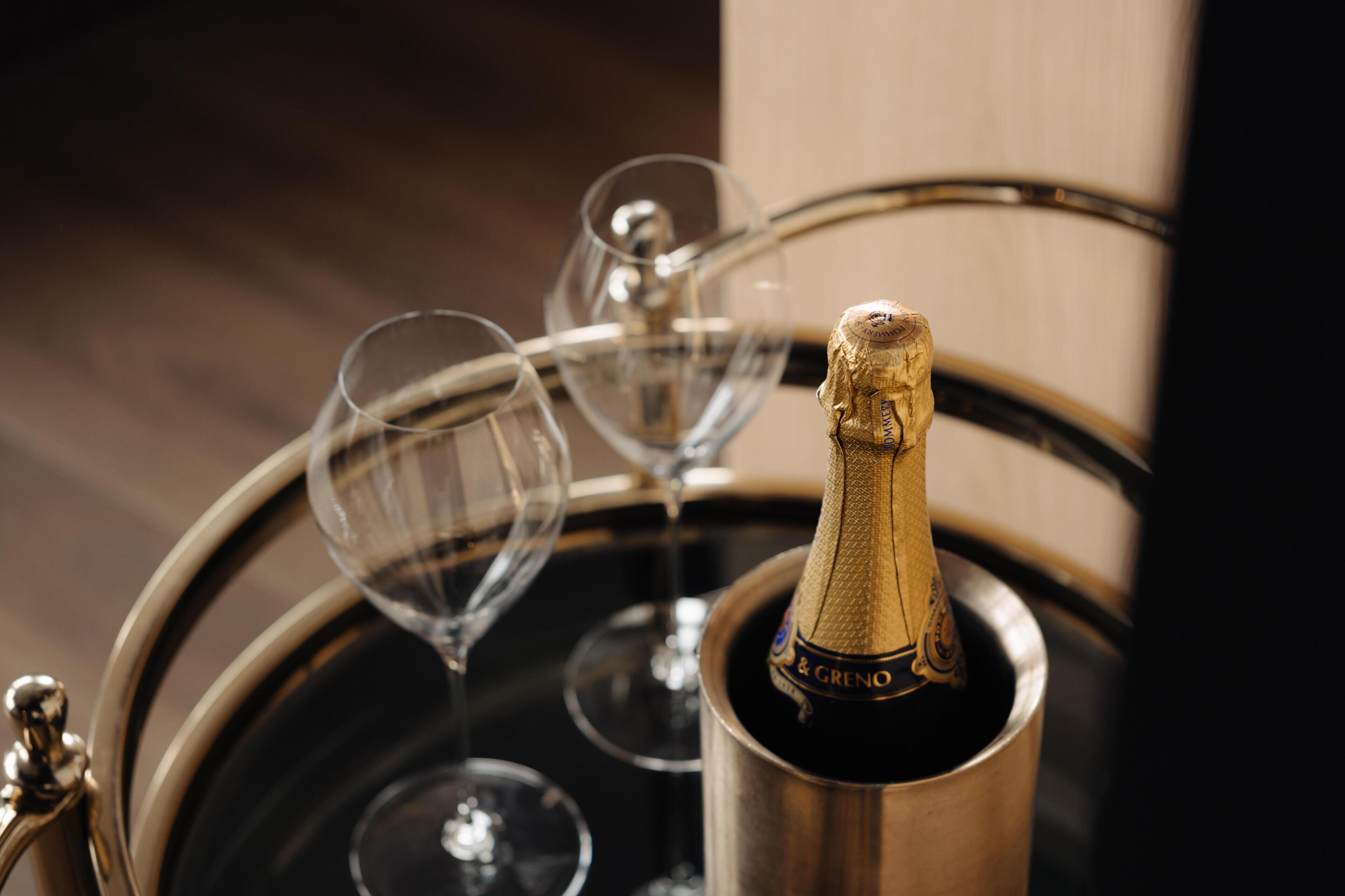 Une bouteille de champagne dans un seau en métal, avec des verres à vin vides.