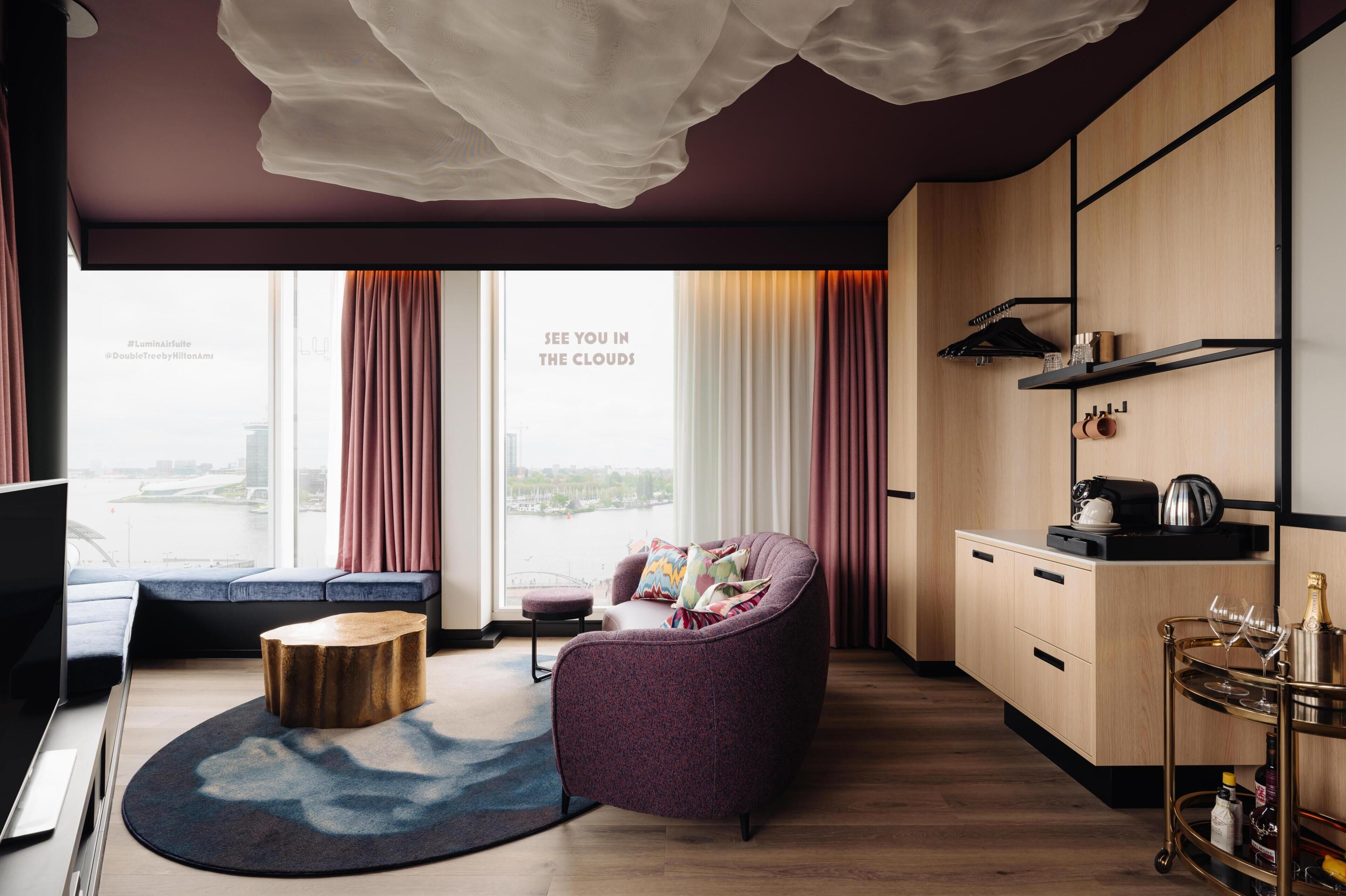 A modern living room with a sofa, a round coffee table, and a view of the city through large windows.