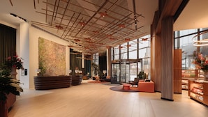 A spacious lobby with a modern ceiling design, a large abstract wall art piece, and a seating area with a wooden reception desk.
