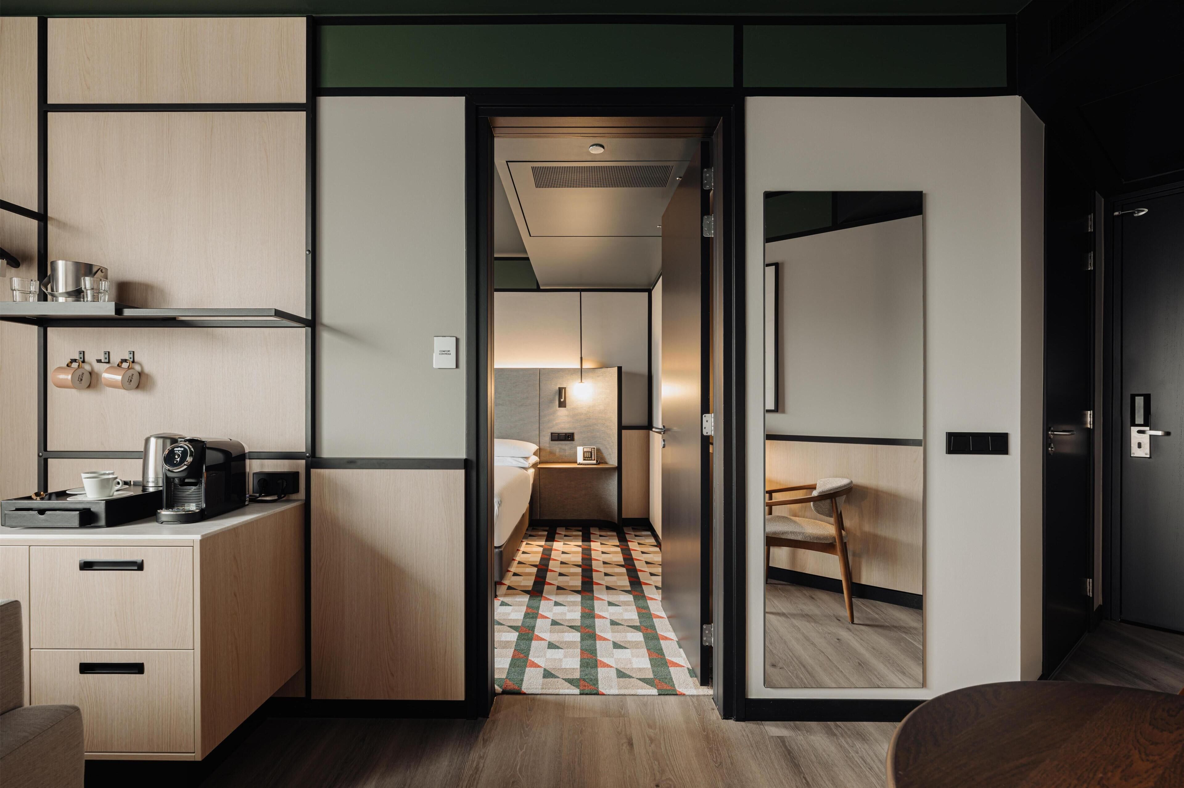 Une chambre d’hôtel compacte comprenant un coin cuisine, une petite salle de bain et un tapis à motifs.