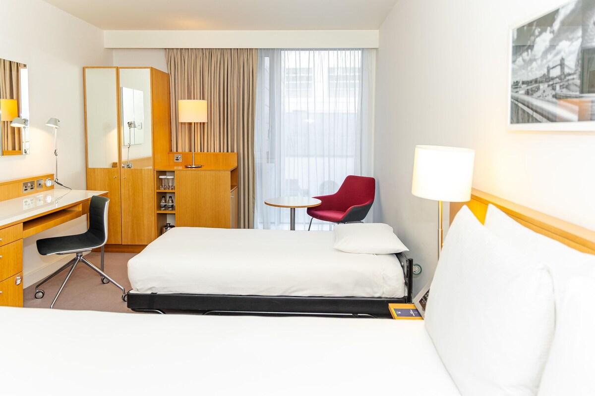 A hotel room with a bed, desk, chair, and a window with curtains.