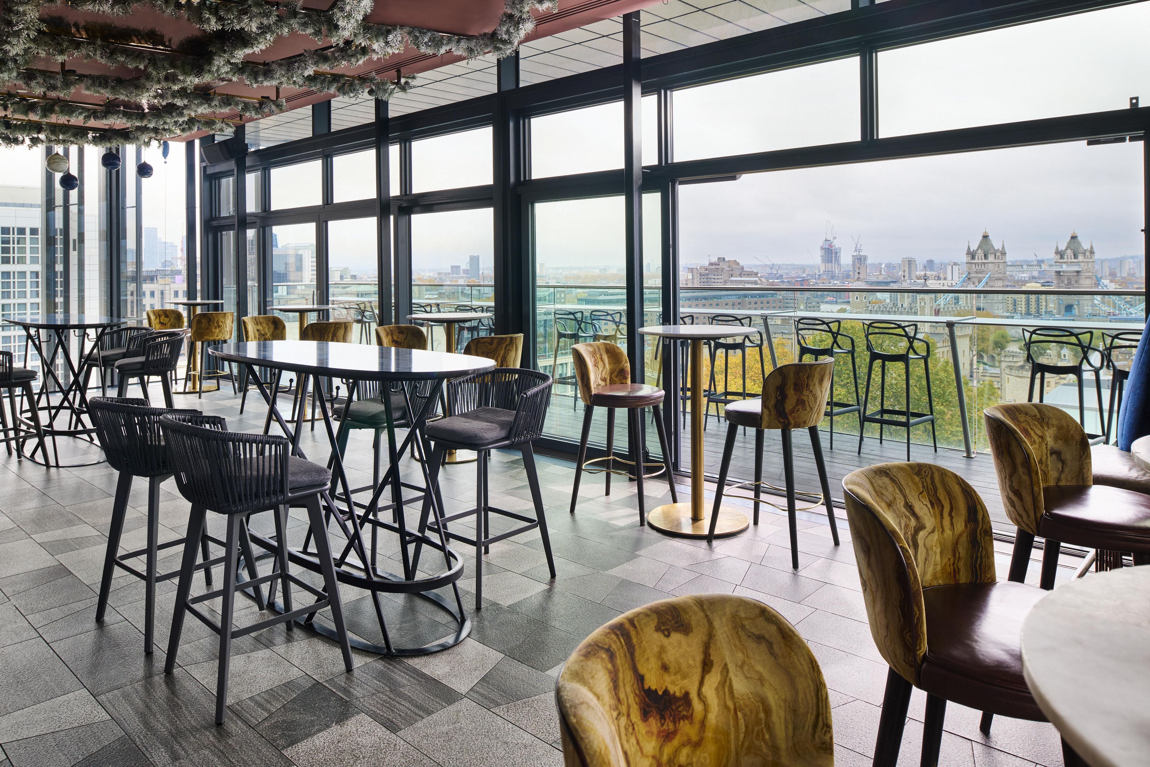 A spacious indoor area with multiple seating arrangements, large windows offering a city view, and a high ceiling with decorative elements.