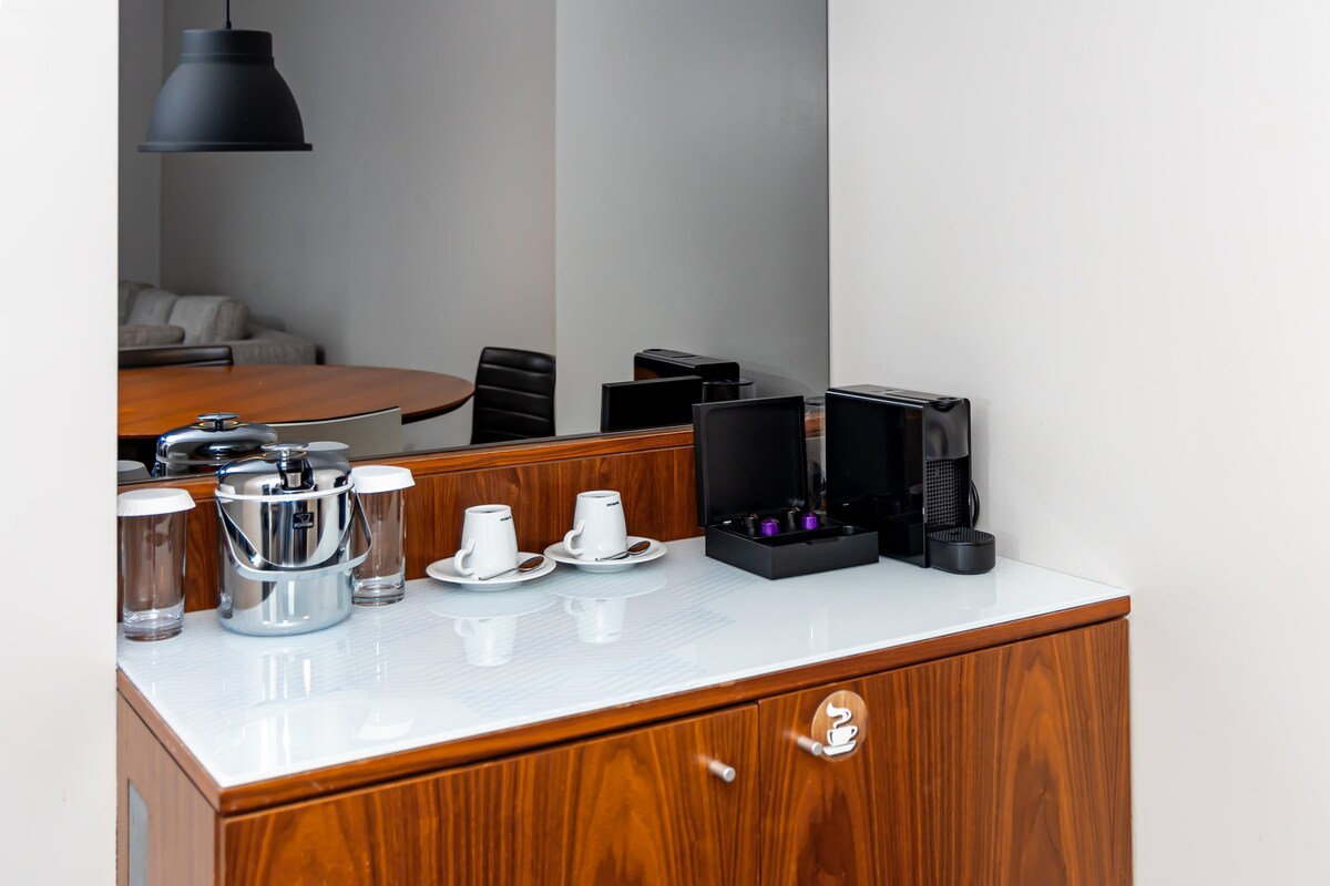 A hotel room with a wooden cabinet, a coffee maker, and two cups on the counter.