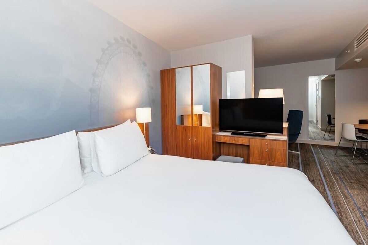 A hotel room with a large bed, a TV, a wooden wardrobe, and a desk with a chair.