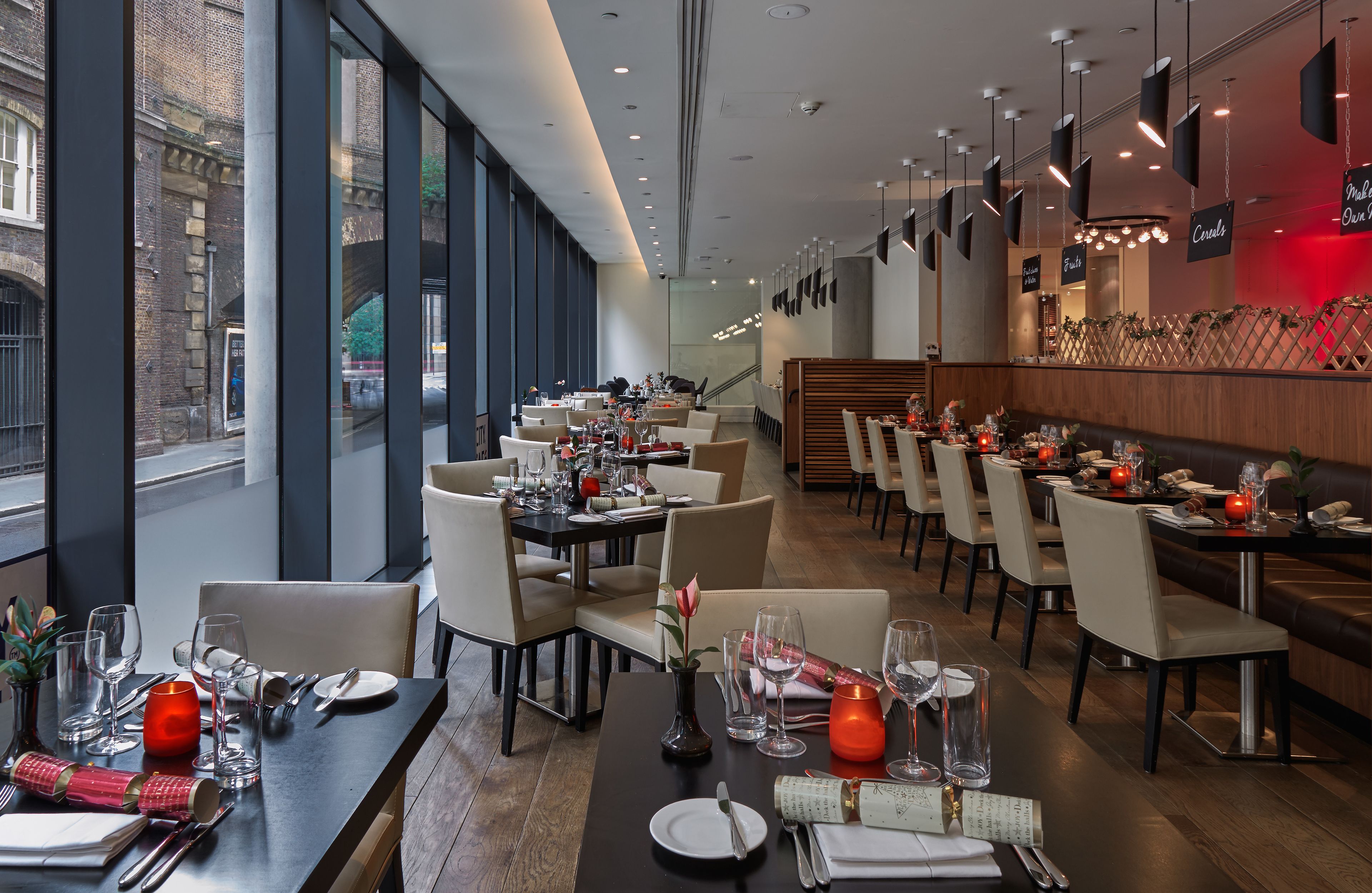A modern restaurant with multiple dining tables and chairs, large windows, and a view of the street.