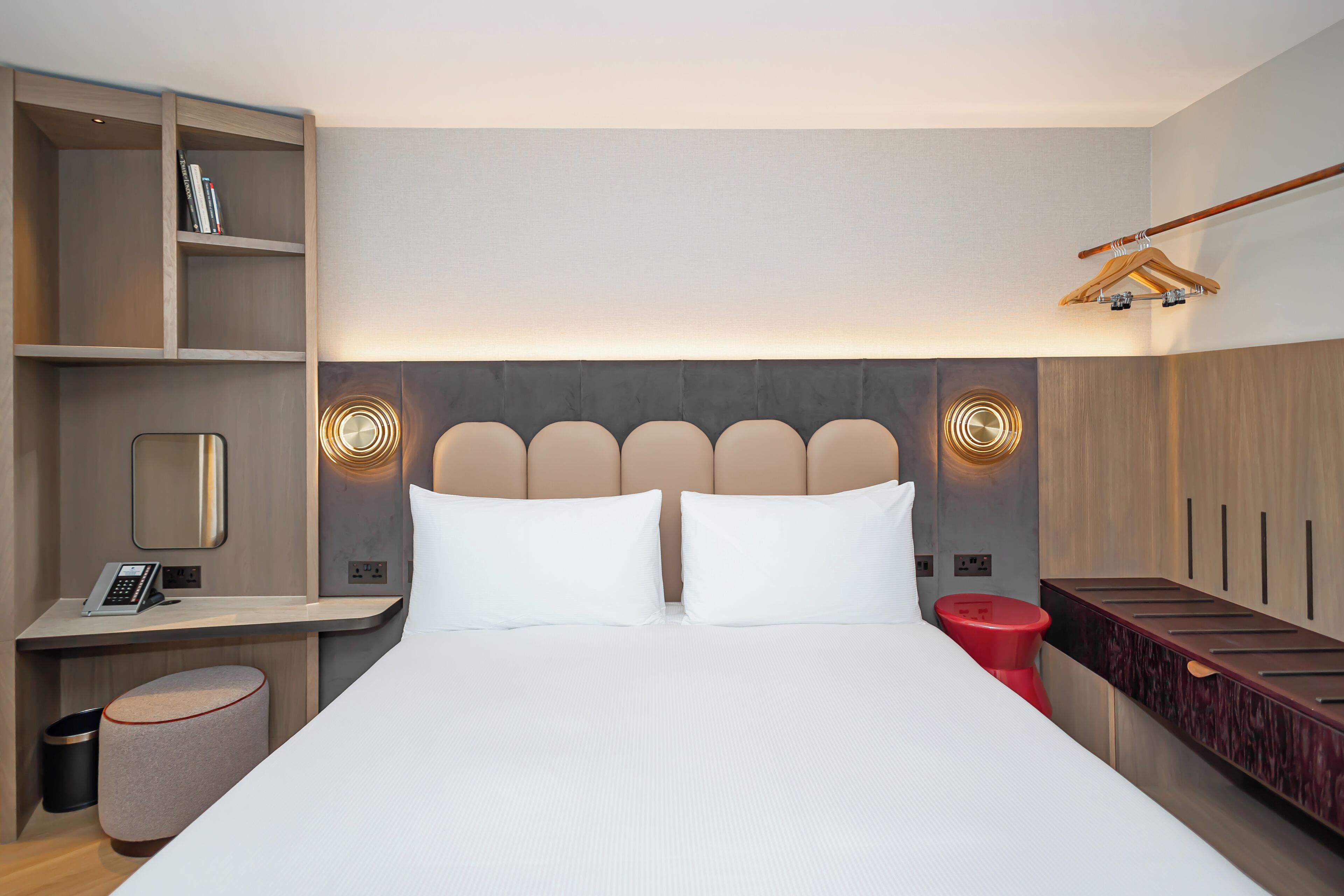 A modern hotel room with a large bed, bedside tables, a wardrobe, and a hanging coat rack.
