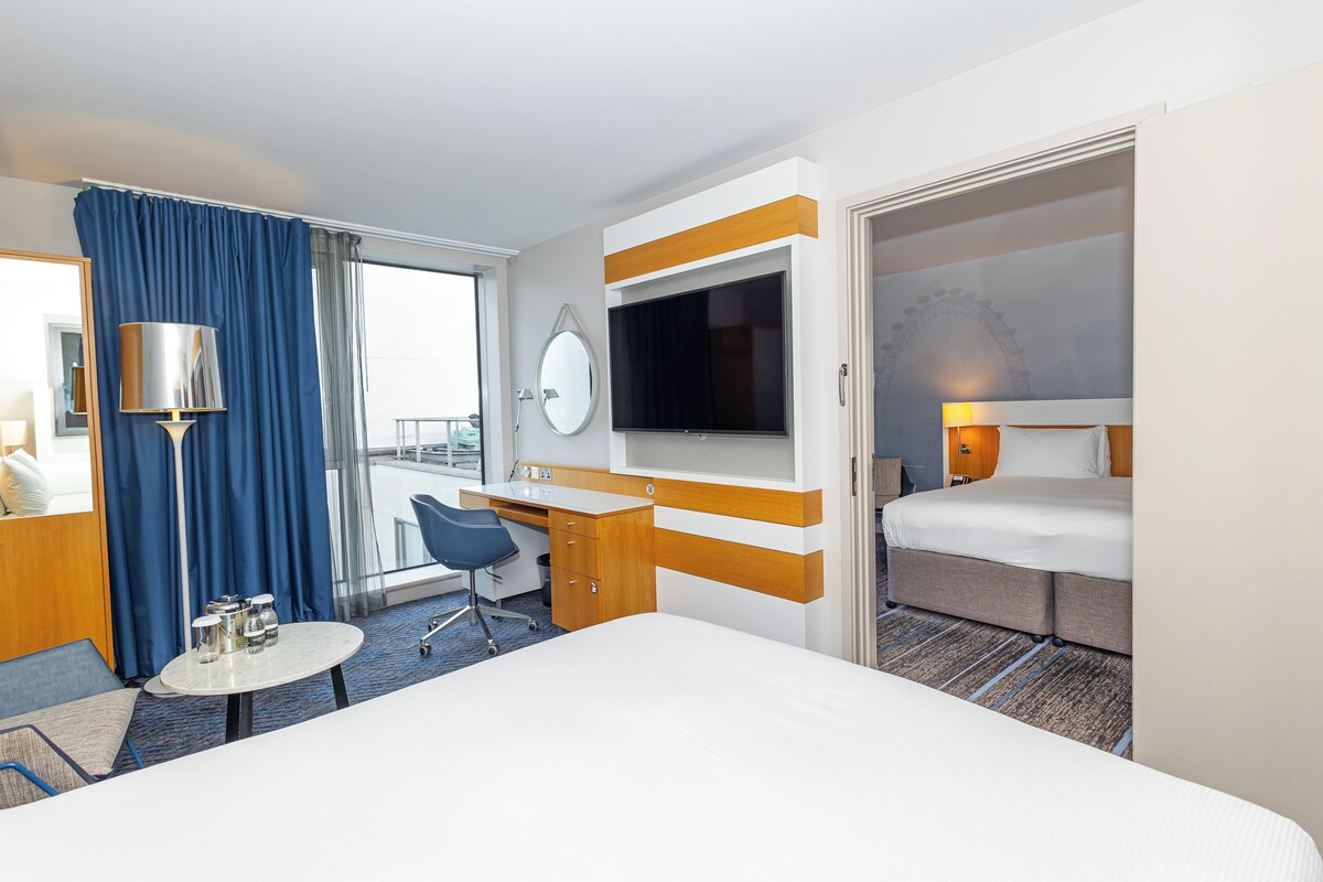 A hotel room with a bed, desk, chair, and a TV mounted on the wall.