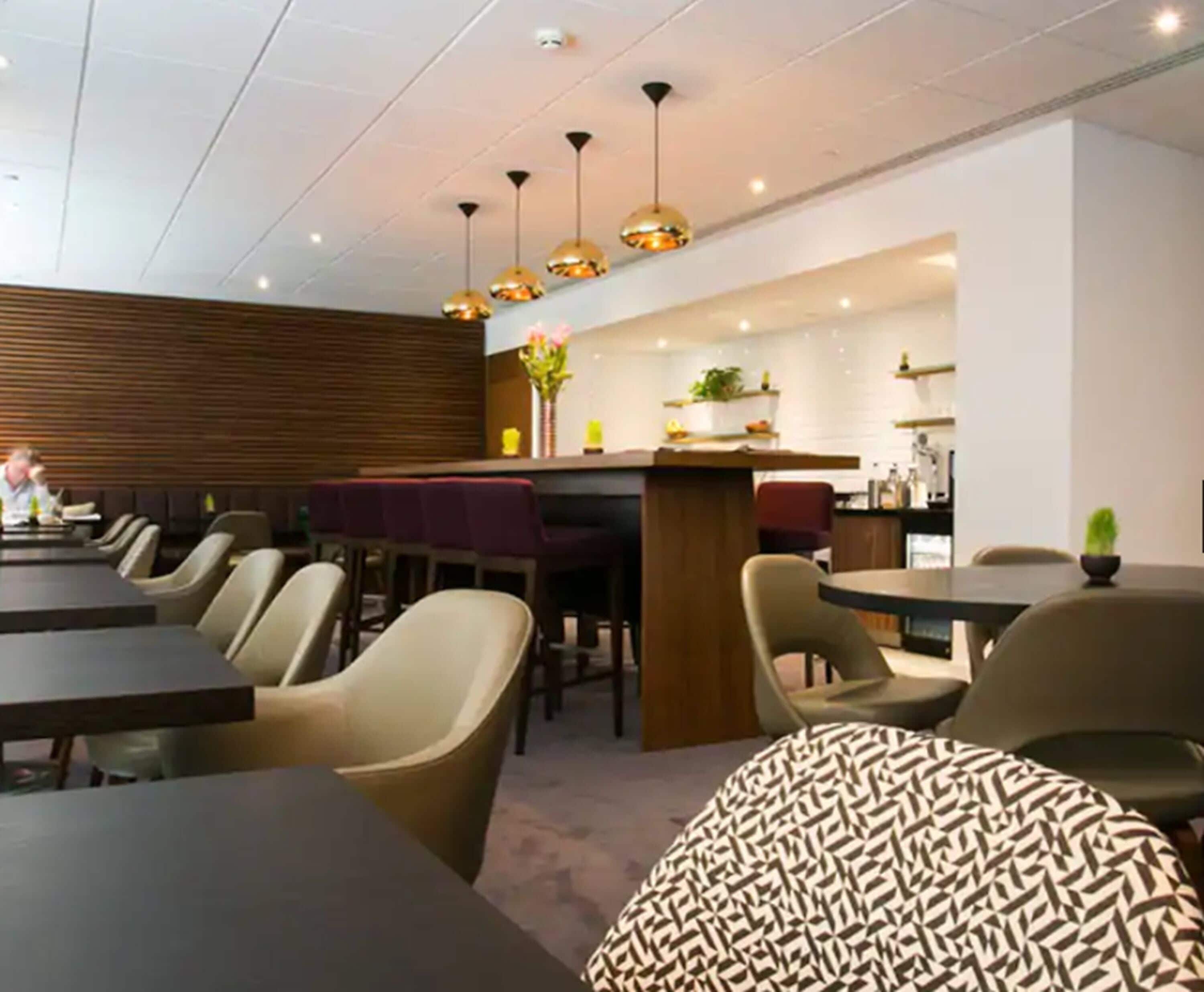 A modern restaurant with long communal tables and individual booths, a bar area, and a visible kitchen.