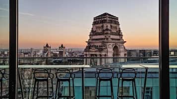 Vista desde un balcón con cuatro sillas, con vistas a una torre histórica y un paisaje urbano al atardecer.