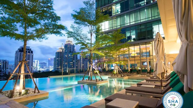 A modern hotel pool area with lounge chairs and a view of the city skyline at dusk. - Sivatel Bangkok (Bangkok)