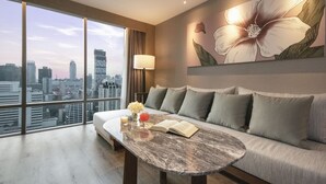 A modern hotel room with a large window offering a city view, a sofa, a marble coffee table, and a floral wall art piece. - Sivatel Bangkok (Bangkok)