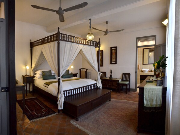 A four-poster canopy bed with a nightstand, a chair, a desk, and a vanity with a mirror. - Satri House (Luang Prabang)