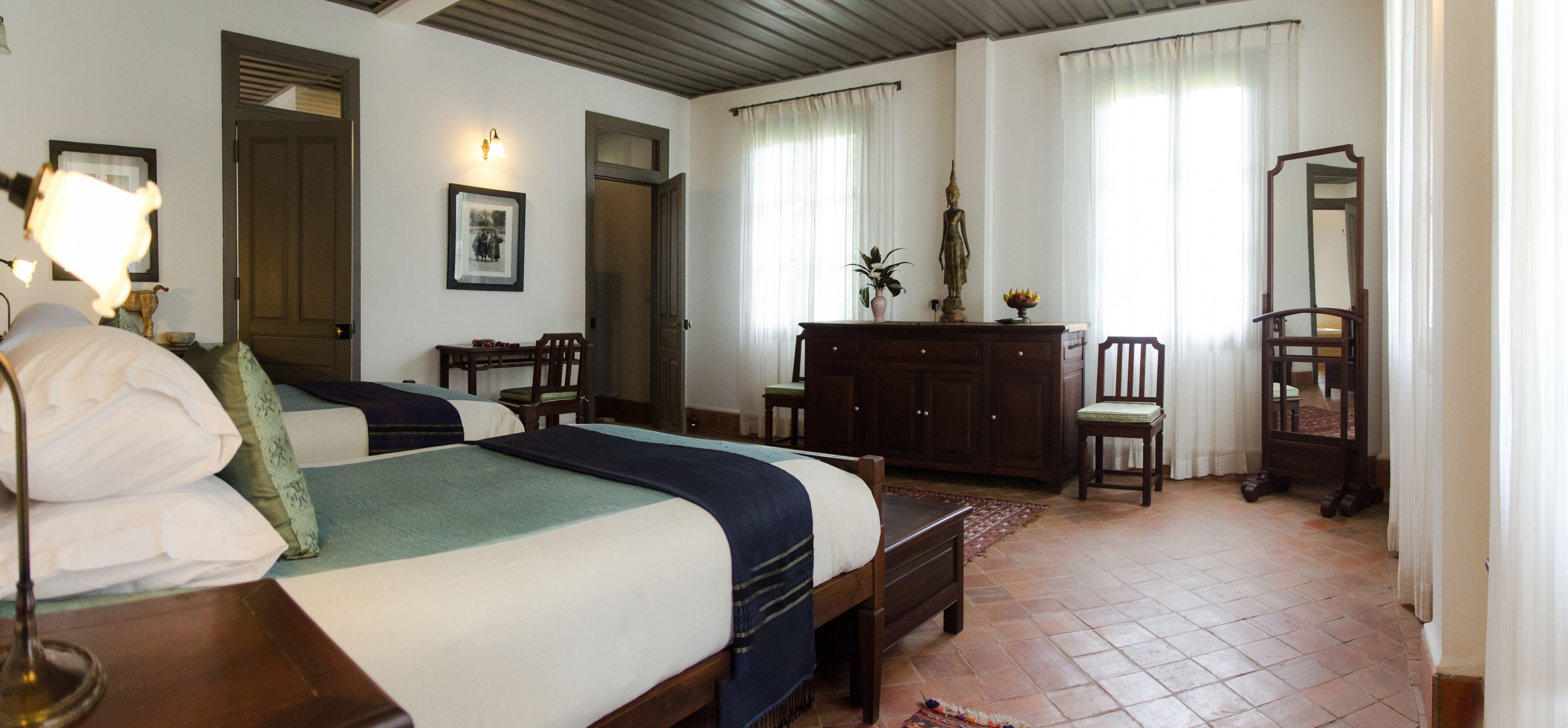 Habitación de hotel con dos camas, un aparador de madera, un espejo y un escritorio con lámpara.