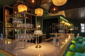 A bar area with shelves of glasses, a bar counter, and green upholstered chairs. - Satri House (Luang Prabang)