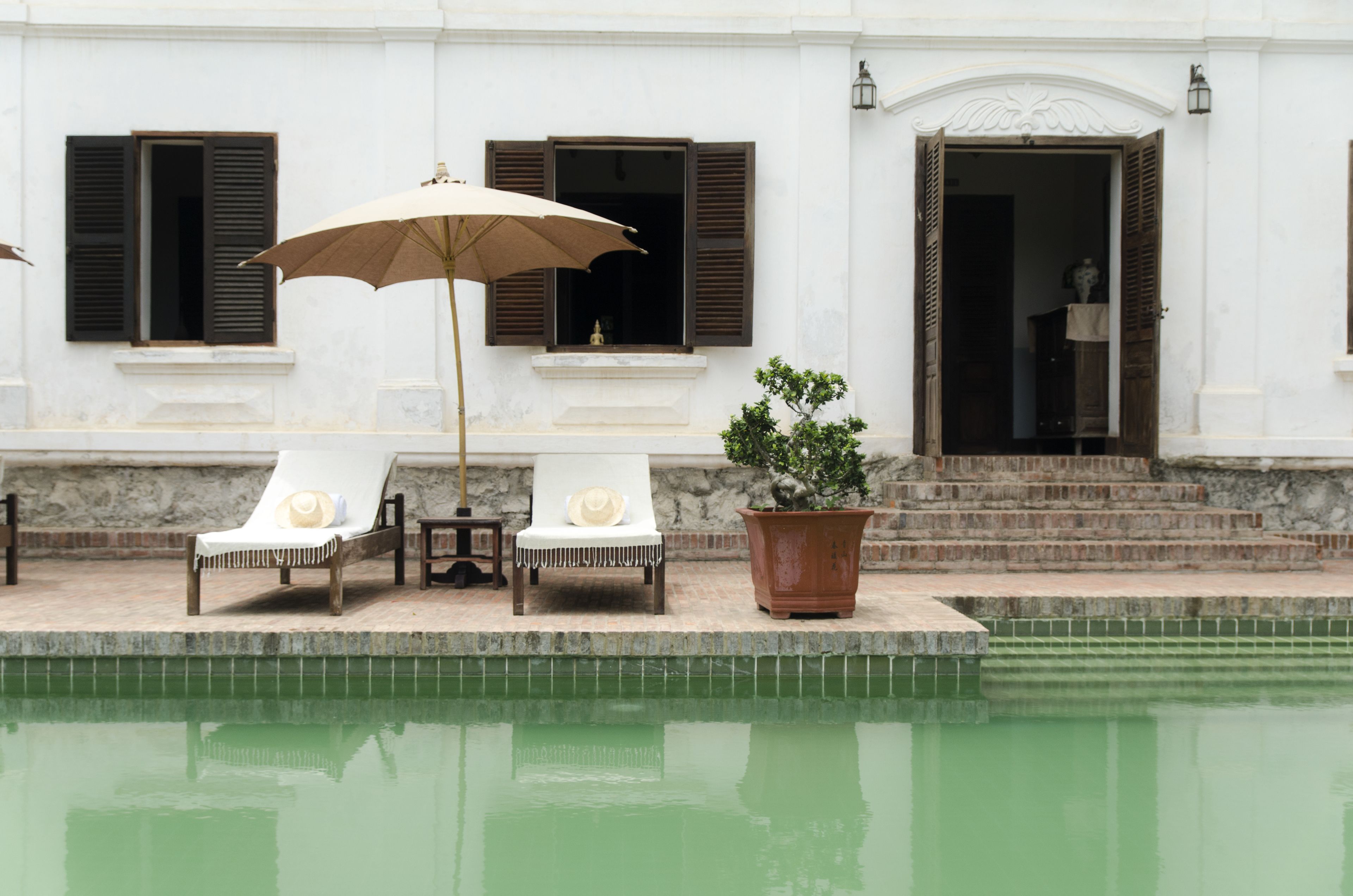 Un espace aménagé au bord de la piscine, comprenant deux chaises longues, une table et un pot de fleurs.