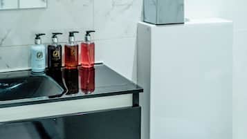 Une salle de bain avec un lavabo en marbre blanc, un plan de toilette noir et des toilettes blanches. On peut voir quatre bouteilles de savon liquide sur le lavabo.