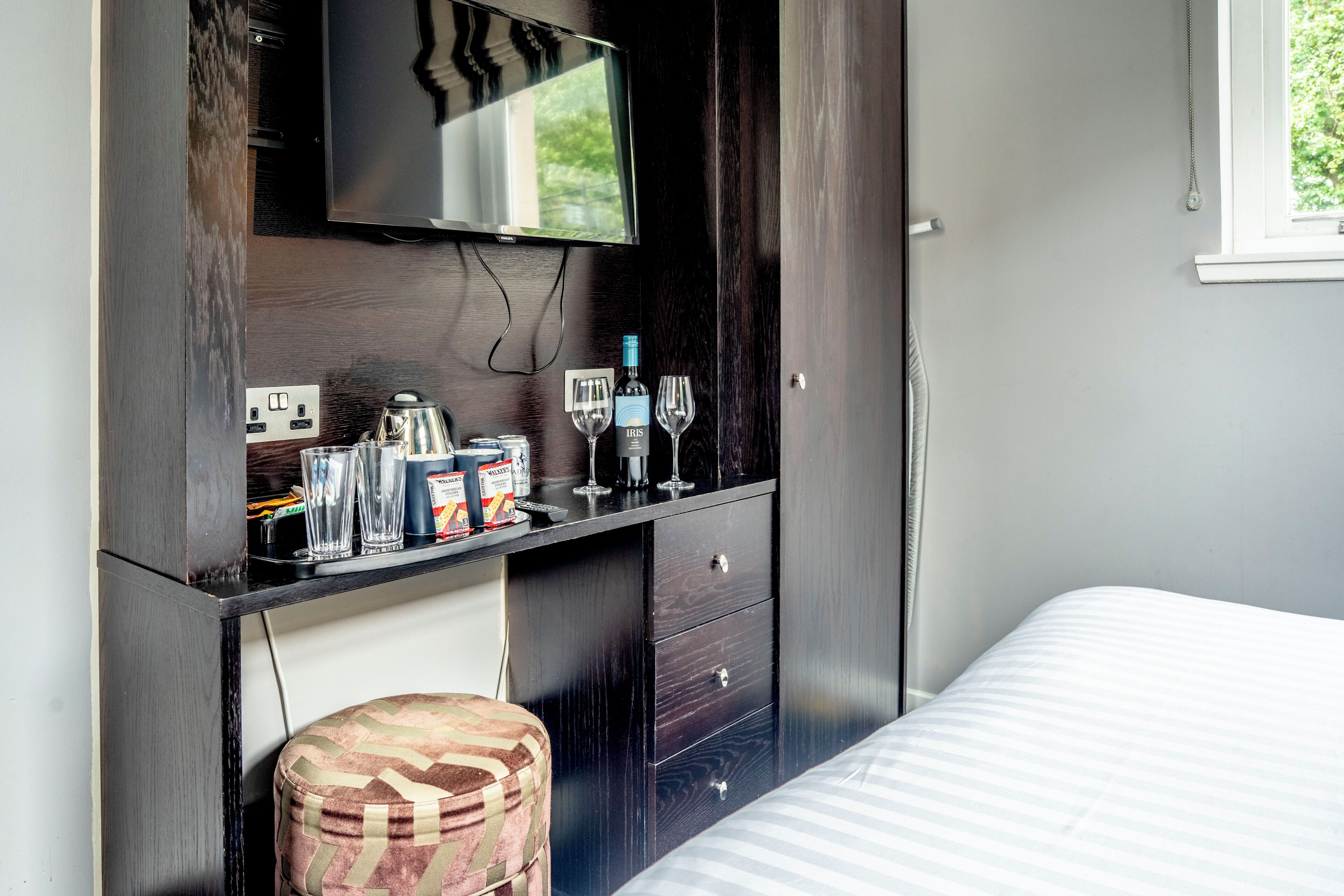 A bedroom with a bed, a desk with a television, and a window.
