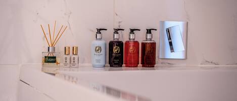 A bathroom with a marble wall, a sink with five bottles of Dove Island shampoo, and a diffuser with reed sticks.