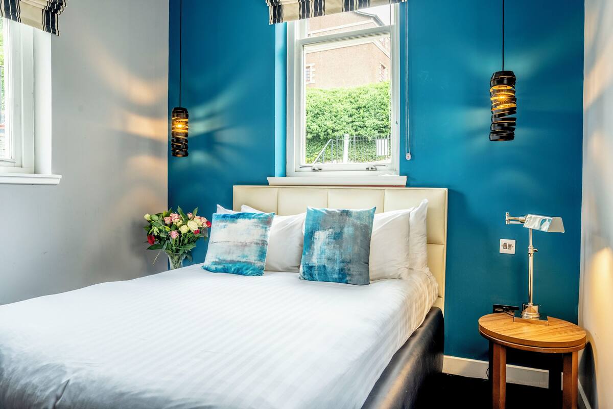 Une chambre à coucher avec un lit, une fenêtre, une table de chevet et une lampe.