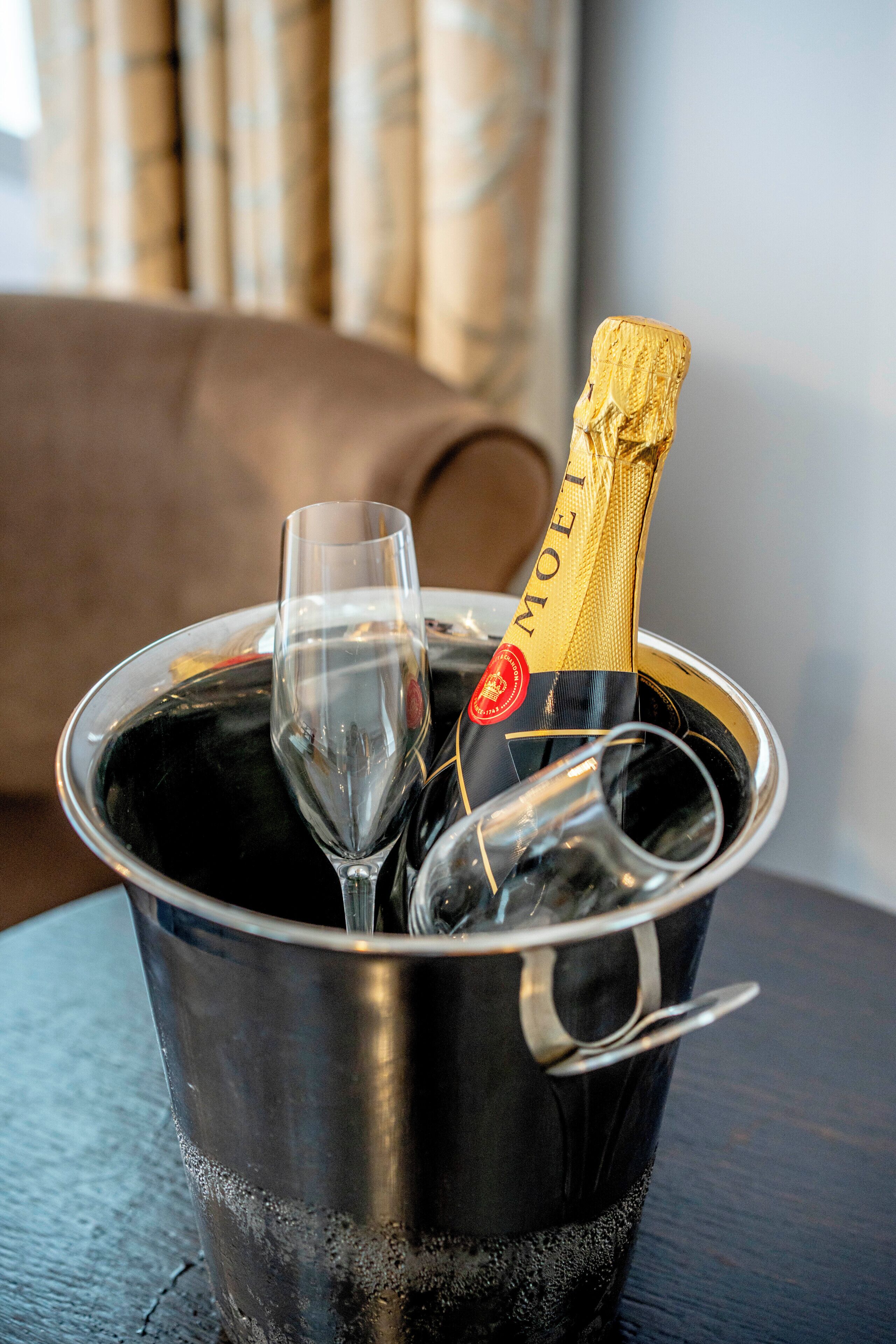 Une bouteille de champagne dans un seau en métal, accompagnée de deux verres.