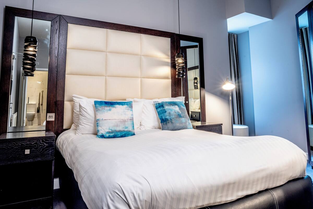 Une chambre d’hôtel moderne avec un grand lit, une tête de lit en bois foncé et un grand miroir.