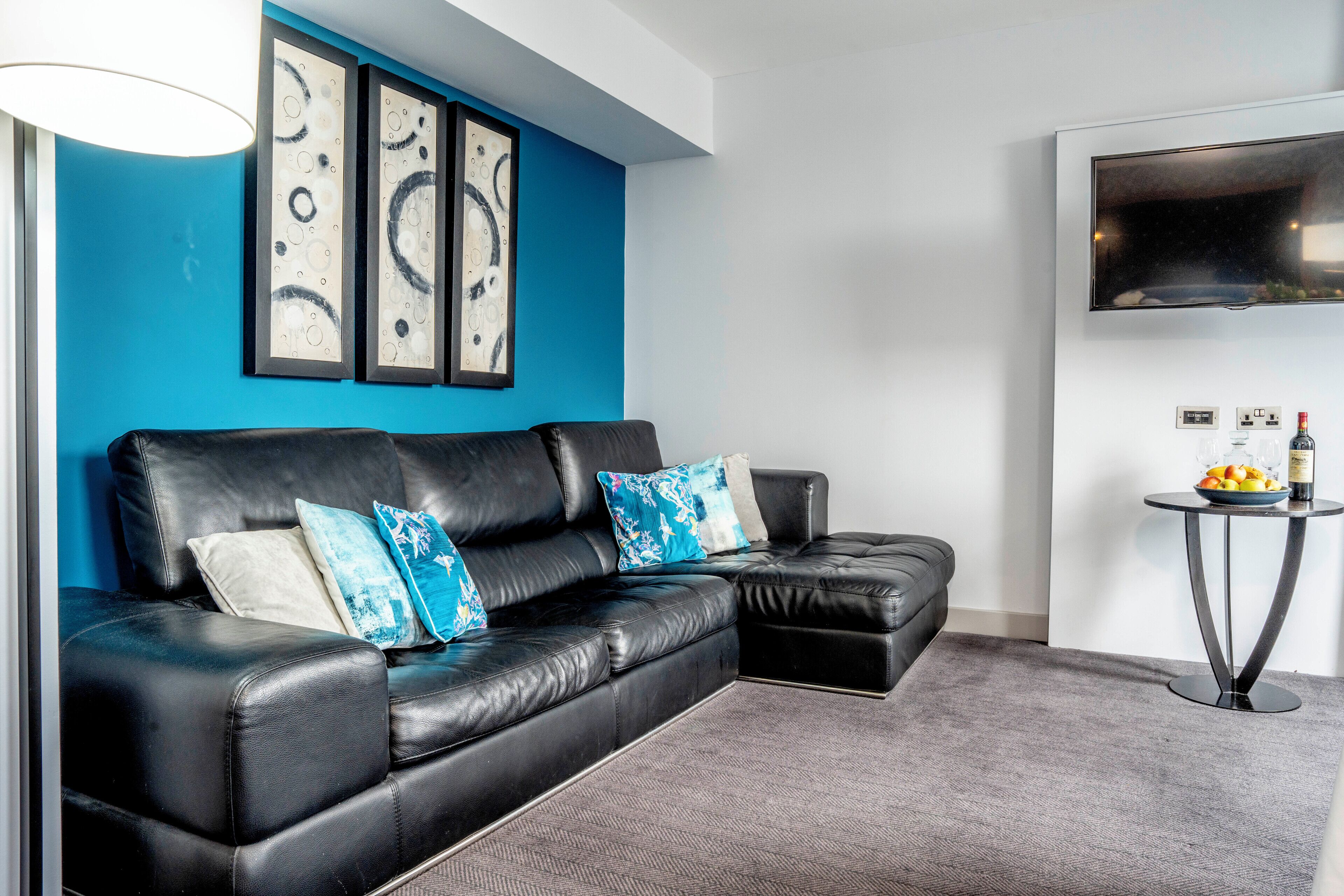 Una sala de estar moderna con un sofá de cuero negro, almohadones azules decorativos y arte abstracto en la pared.