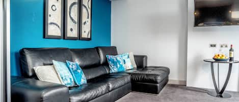 Una sala de estar moderna con un sofá de cuero negro, almohadones azules decorativos y arte abstracto en la pared.