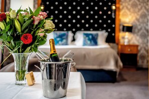 A hotel room with a bed, a nightstand, a vase with flowers, and a champagne bottle in a bucket.