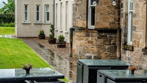 A stone building with a tower, outdoor seating with tables and chairs, and a pathway leading to the entrance. - Colessio (Stirling)